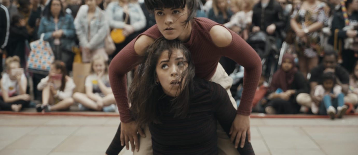 Two female dancers balancing on each others backs in an outdoor performance