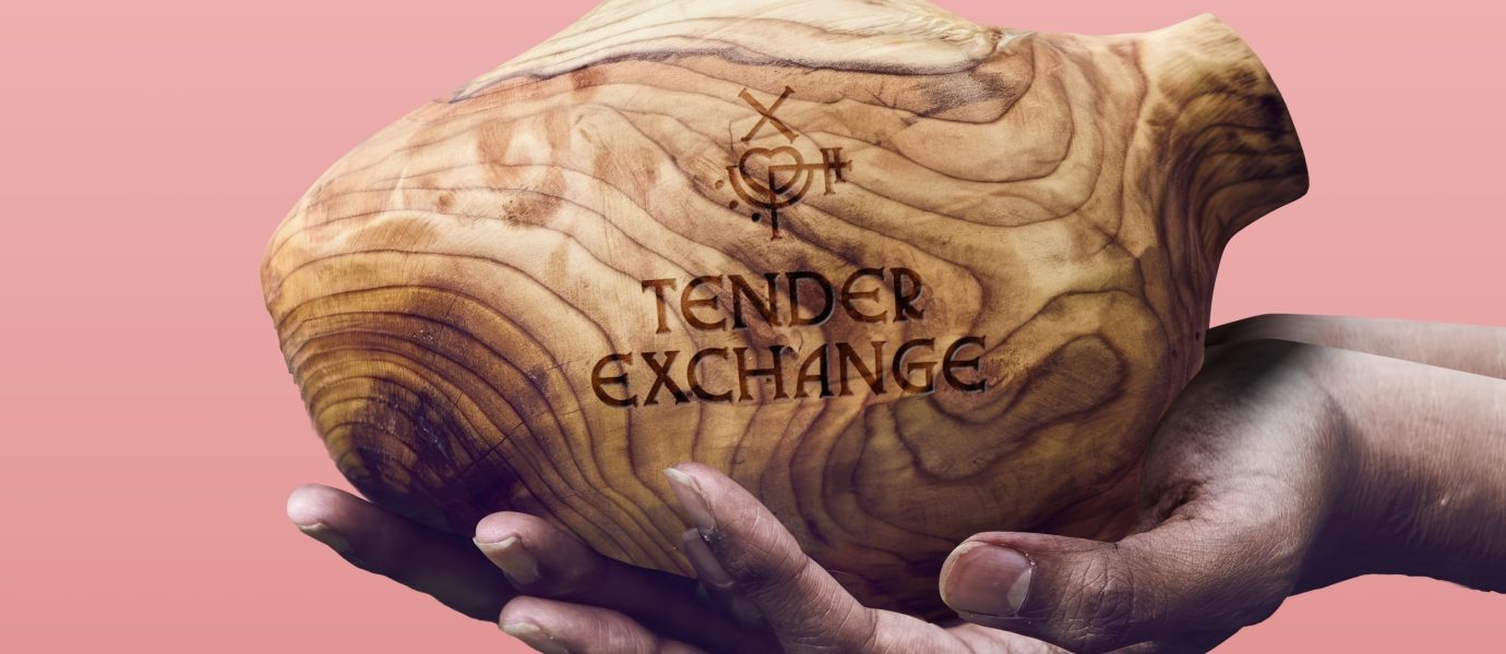 A pair of hands holds a smooth wooden vessel with natural grain patterns. The vessel is engraved with the words TENDER EXCHANGE and a symbol, all against a pink background.