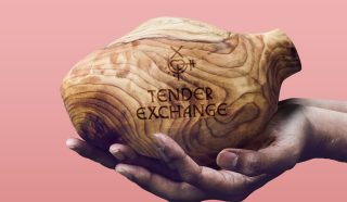 A pair of hands holds a smooth wooden vessel with natural grain patterns. The vessel is engraved with the words TENDER EXCHANGE and a symbol, all against a pink background.